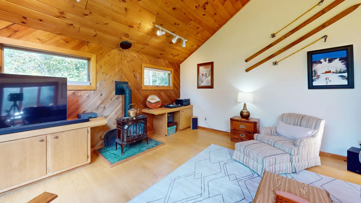 A cozy lounge area with a prominent wood-burning stove, an accent chair, decorative wall art, and a large TV. The warm lighting and textures create a welcoming space ideal for curling up by the fire or enjoying a movie night.