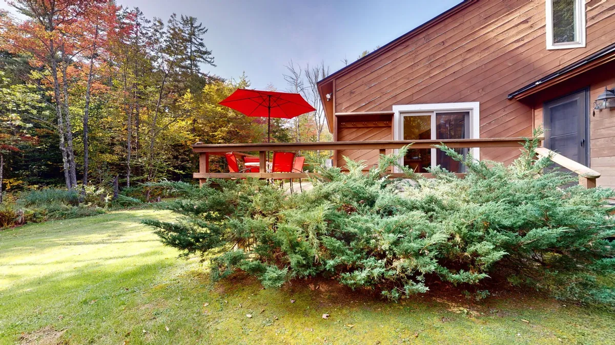 This photo showcases a wooden deck furnished with vibrant red chairs and a red umbrella, surrounded by lush greenery. The cheerful setup hints at shared family meals outdoors or quiet moments in nature, reinforcing the possibilities for relaxation and togetherness in the fresh Vermont air.