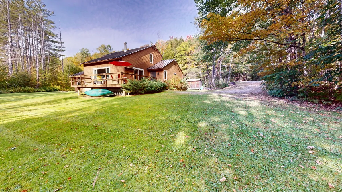 An inviting view of a wooden deck surrounded by greenery, with a lawn area, nearby outdoor storage shed, and mature trees. The deck is ideal for enjoying the outdoors, whether for barbecuing, soaking up nature, or preparing for a day at the resort.