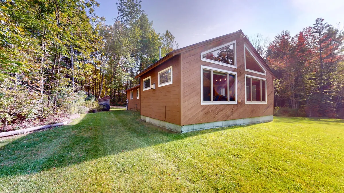 The property’s wooden exterior with large windows overlooks a lush green lawn, offering a serene and inviting first impression. The setting suggests opportunities for outdoor gatherings and taking in sunsets after a day on the mountain.
