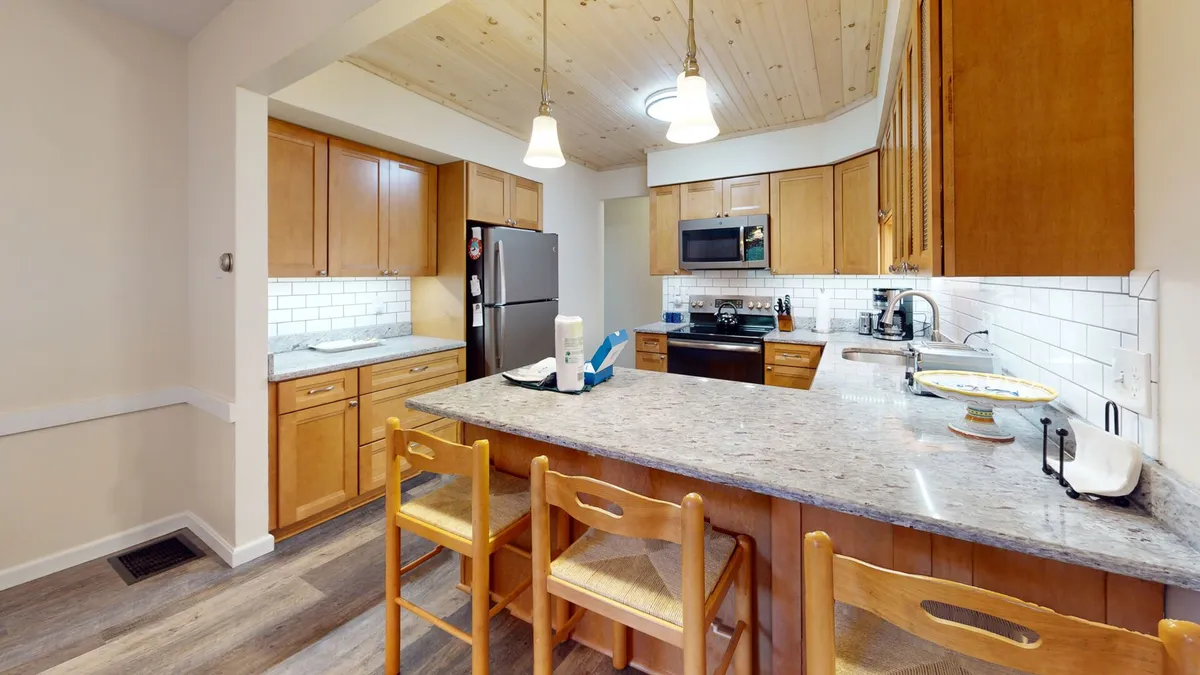 A sunlit, recently renovated kitchen featuring a granite countertop, wooden cabinets, a spacious kitchen island, and modern appliances. The setup is open and inviting, perfect for cooking and entertaining multiple guests.