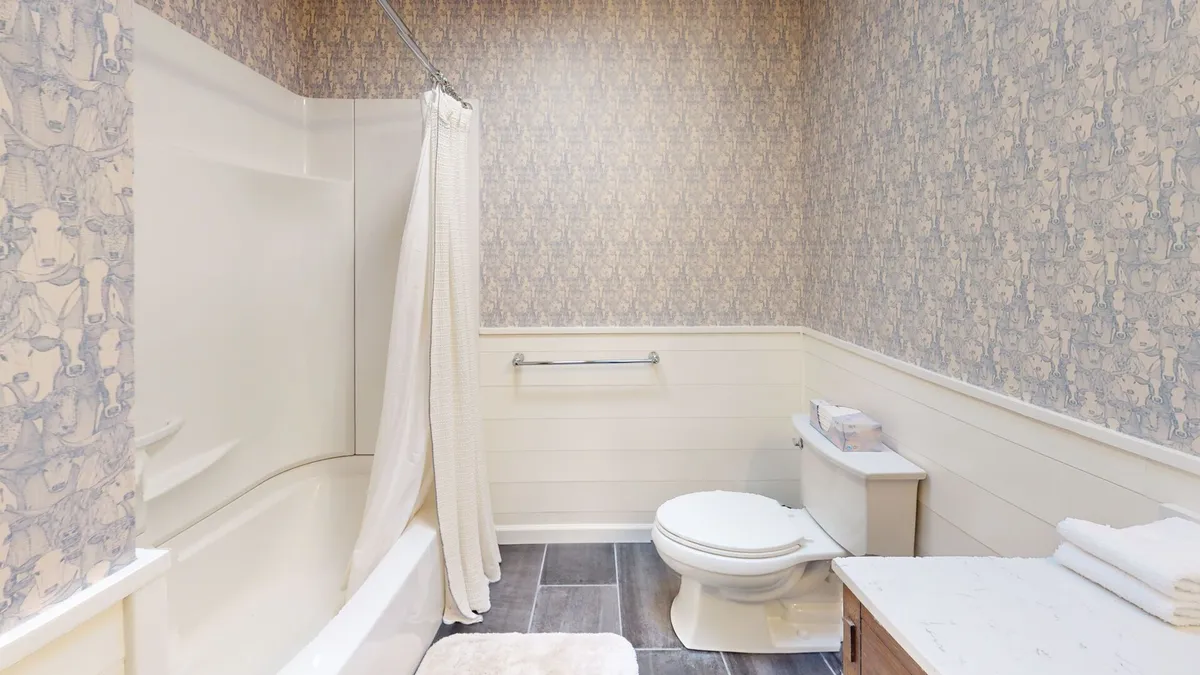 A tranquil bathroom scene with a clean white bathtub, toilet, and a vanity topped with plush towels. Soft lighting and uncluttered surfaces set a soothing mood, inviting guests to unwind with a relaxing bath or refresh after a day of exploration.