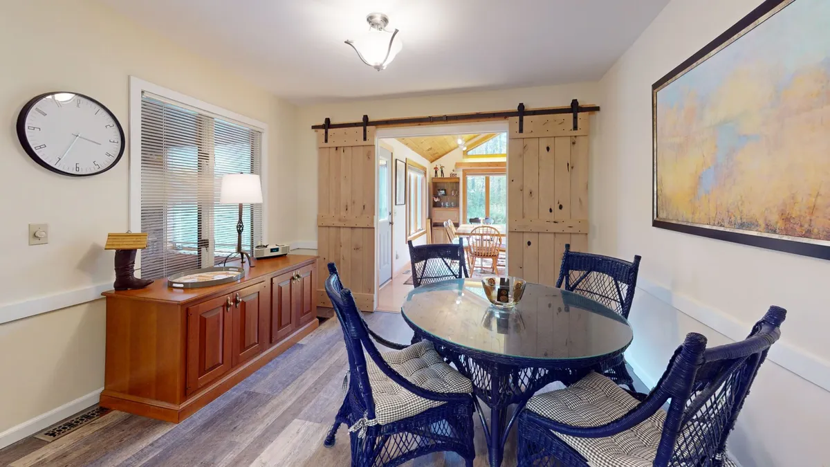 This interior image features a round glass table surrounded by blue wicker chairs and wooden sliding doors, creating a warm, welcoming space for meals, games, or casual conversations.