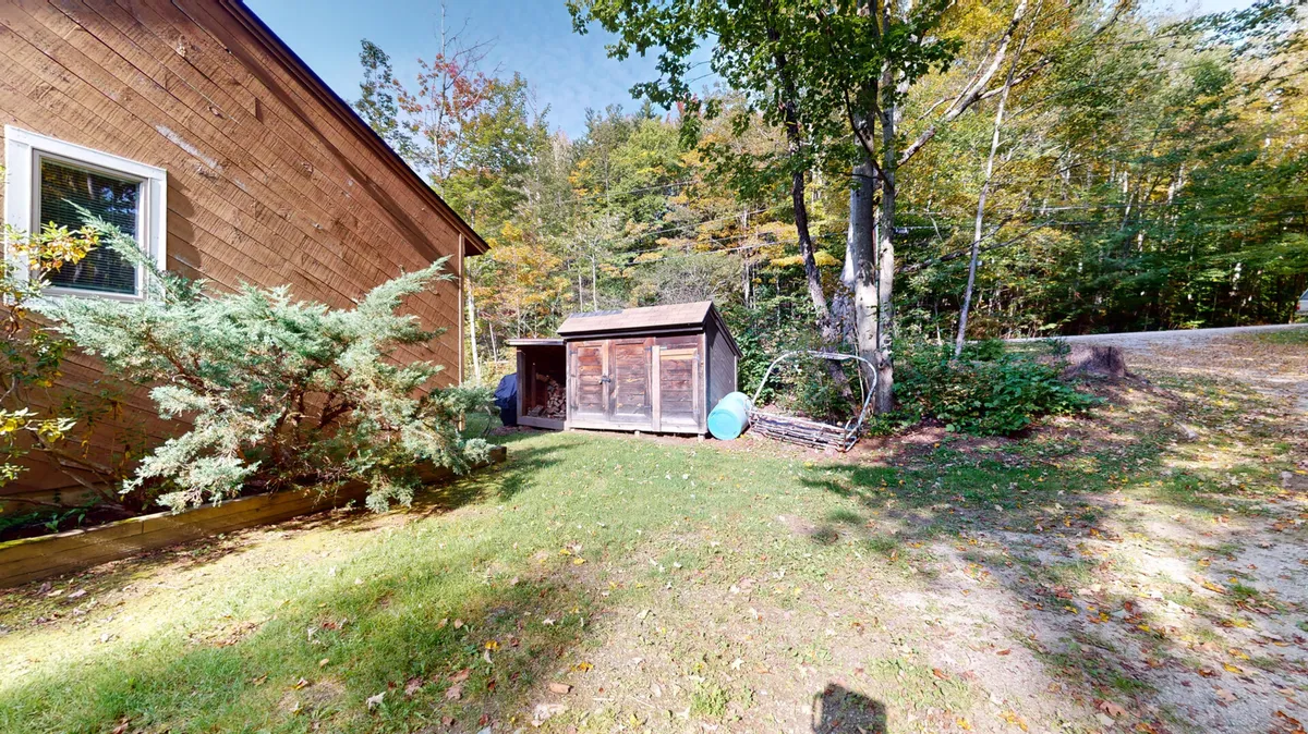 The image captures a peaceful scene with a storage shed, lush greenery, and a dirt path leading through the yard. The natural setting hints at opportunities for children to explore and play, while adults can relax amid serene surroundings.