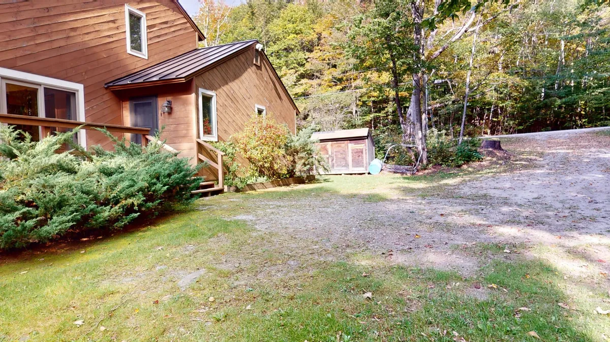 This image displays the exterior of The Maple Leaf, showcasing its wooden siding, a well-maintained garden, and a storage shed. The scene suggests a peaceful outdoor environment ideal for gatherings and relaxation after a day of mountain or golf adventures.