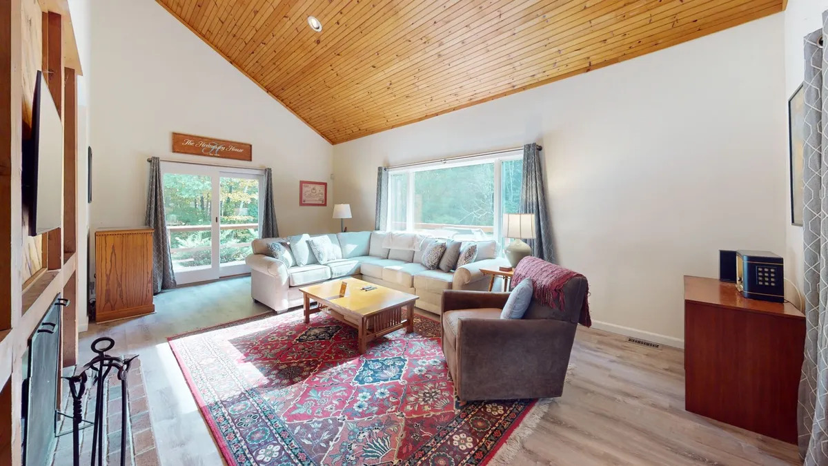 A welcoming great room with a comfortable sofa, ornate rug, wooden ceiling, and large windows that flood the space with natural light. The room is ideal for relaxing, socializing, and celebrating special moments with groups.